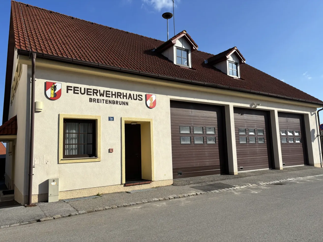 Die Vorderseite eines Feuerwehrhauses mit zwei Garagen, einem Fenster und der Aufschrift 'Feuerwehrhaus Breitenbrunn' an der Wand.