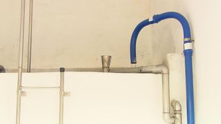 Eine Nahaufnahme eines blauen Rohres, das an einer weißen Wand befestigt ist. In der Mitte des Rohres ist ein metallischer Trichter befestigt.