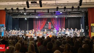 Ein Live-Auftritt der Old School Basteards auf einer Bühne mit roten Vorhängen und Lichtern. Das Publikum sitzt vor der Bühne und beobachtet die Band.