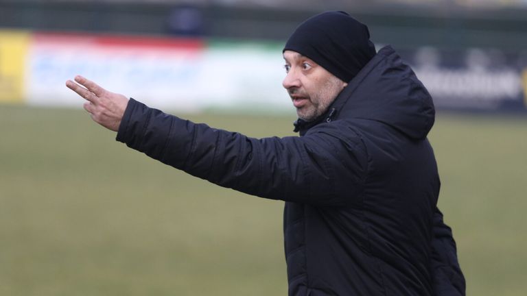 Ein Mann in einer schwarzen Jacke und Mütze deutet auf einem Feld, wahrscheinlich Anweisungen oder Richtungen gebend.