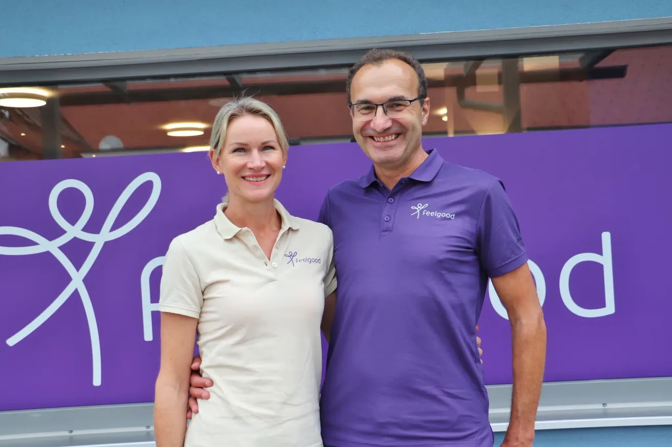 Ein Mann und eine Frau stehen nebeneinander, lächeln und posieren für ein Foto vor einer lila Wand.