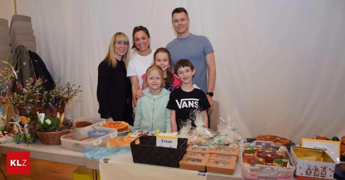 Eine Familie von fünf posiert vor einem Tisch mit verschiedenen Gebäckstücken, eine Frau hält ein Schild mit der Aufschrift 'Freie'.