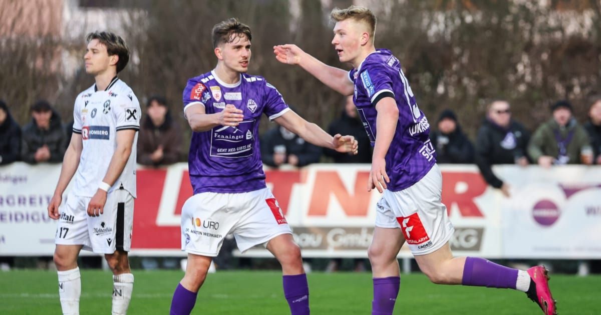 Zwei Fußballspieler in lila und weißen Trikots feiern ein Tor auf dem Feld, während ein dritter Spieler in Weiß hinter ihnen steht.