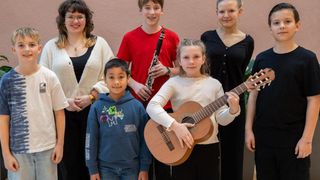 Eine Gruppe junger Musiker steht zusammen. Ein Mädchen hält eine Gitarre, ein Junge spielt Klarinette und andere lächeln für die Kamera.