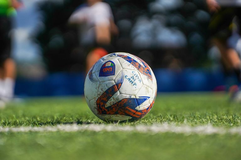 Ein Fußball mit 'CITY CAMP' darauf, bedeckt mit Schmutz, liegt auf einem grünen Feld.