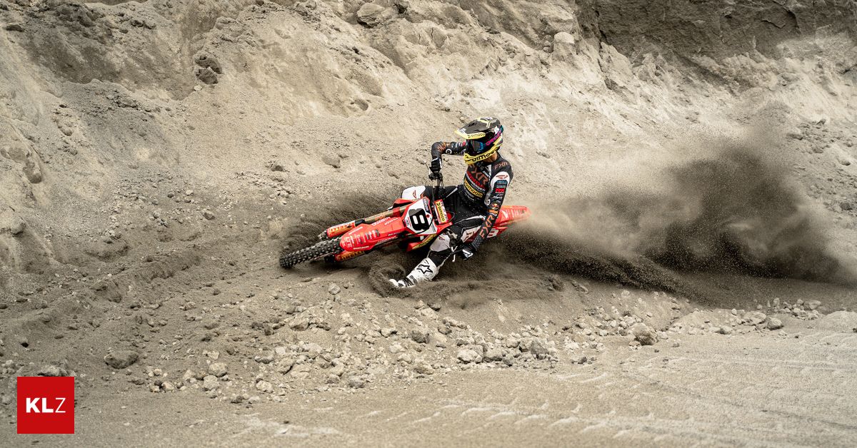 Ein Motocross-Fahrer fährt auf einer roten Maschine und wirft Staub auf einer Schotterpiste auf. Der Fahrer trägt einen Helm und einen Rennanzug.