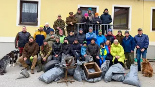 Eine Gruppe von Menschen in Winterkleidung posiert für ein Foto vor einem Haus mit Säcken voller Müll. Einige stehen auf einem Balkon, andere sitzen.