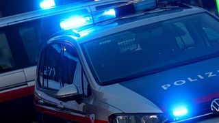 Ein Polizeiauto mit blauen Lichtern auf dem Dach ist nachts geparkt. Das Wort 'POLIZEI' ist vorne sichtbar.