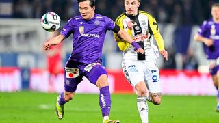 Zwei Fußballspieler kämpfen bei einem Spiel um den Ball. Einer trägt ein lila Trikot, der andere ein gelb-weißes Trikot.