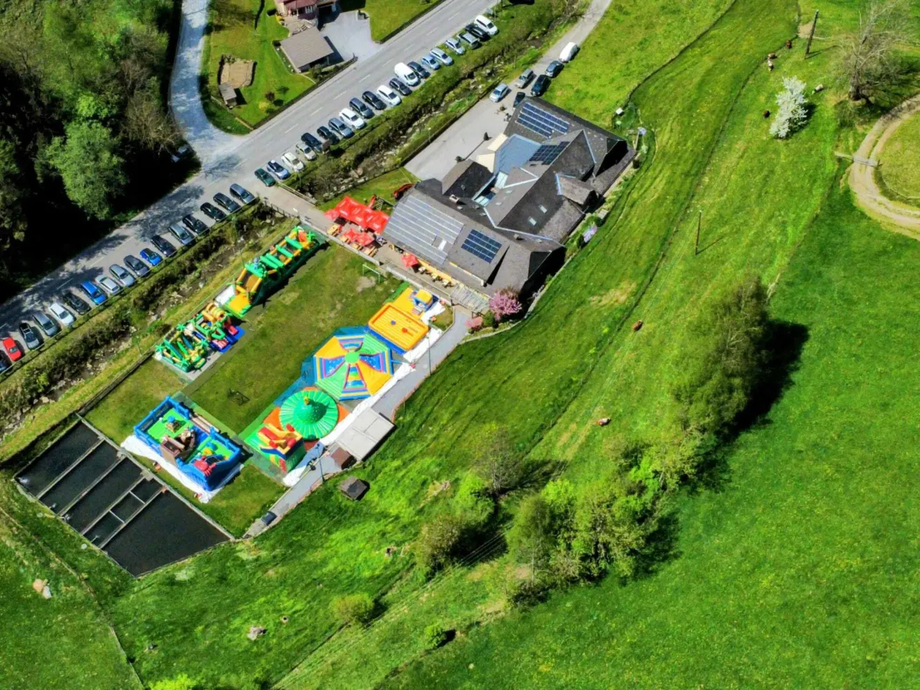 Aerial view of a colorful playground with bouncy houses and slides. Nearby, there are houses and a parking lot with solar panels on the roofs.