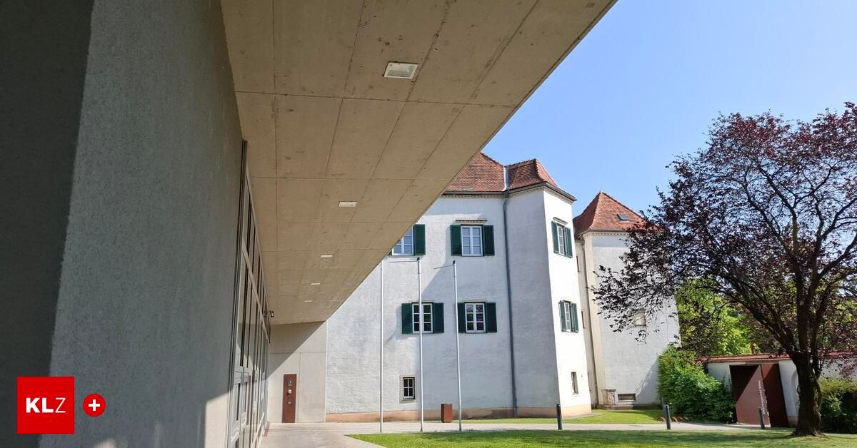 An outdoor view of a building with glass windows and a concrete awning. A flagpole is on the lawn in front.