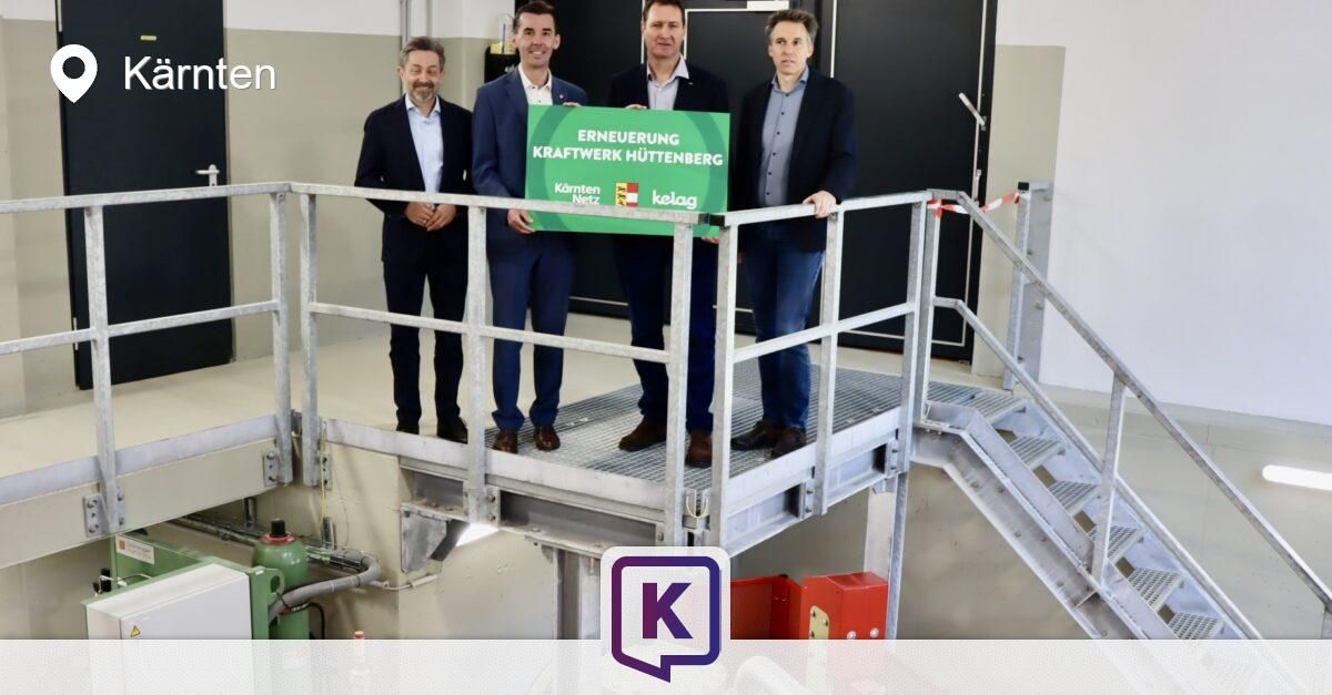 Four men stand on a metal platform, holding a green sign that reads 'Erneuerung Kraftwerk Huttenberg'. They are dressed formally. The setting appears to be an industrial area.