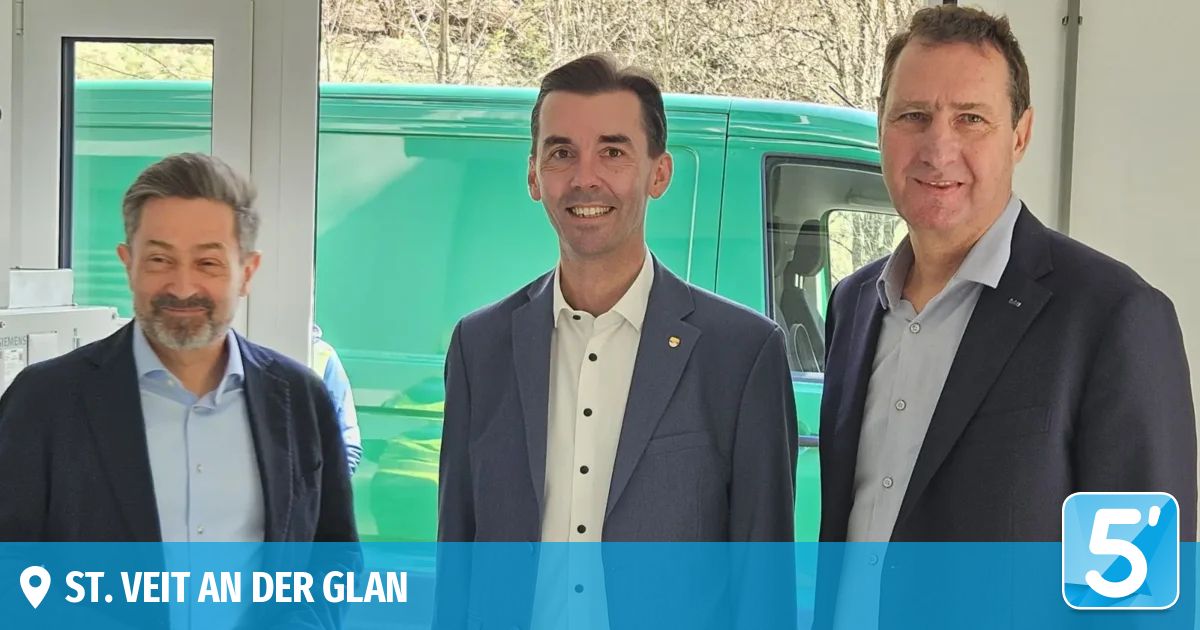 Three men stand in front of a green vehicle, smiling. The man in the middle wears a badge on his blazer. Trees are visible behind them. The text 'N DER GLAN' is at the bottom left.