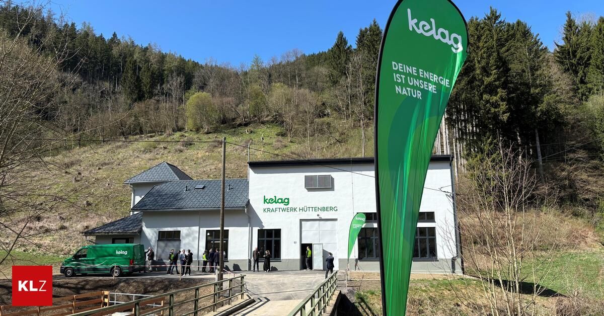 A white building with the word 'kelag' is in front of a green hill. A green banner is in front of it. People are standing in front of the building.