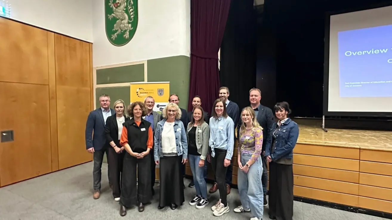 Group photo of people standing in front of a stage, with a lion emblem and a banner behind them. They are smiling for the camera.