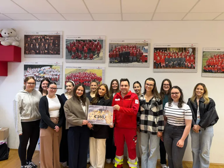 A group of smiling people stand around a man in red, holding a certificate for 350 euros. Behind them, framed photos of groups in red uniforms adorn the wall.