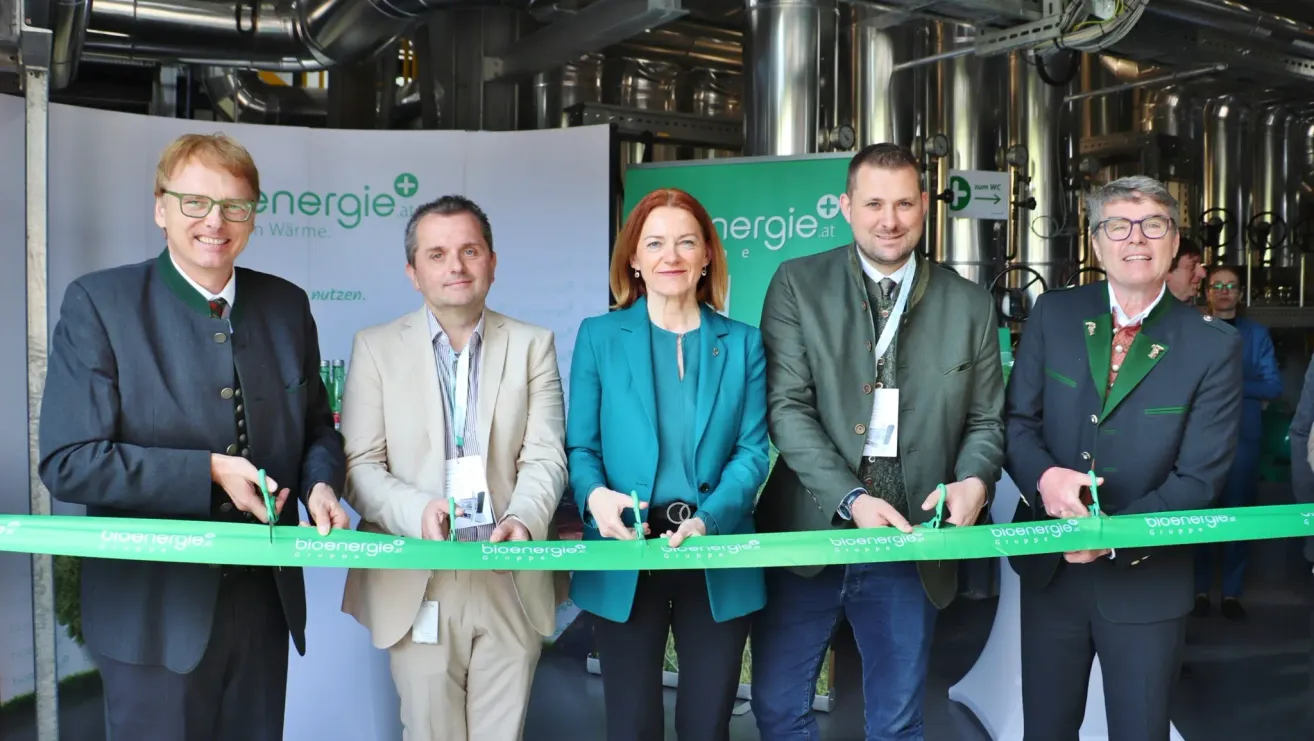 Three people in suits stand next to a woman in a blue blazer, cutting a green ribbon with the word bioenergie at the center. Behind them is a green banner.