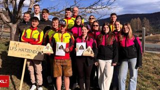 Group photo of individuals dressed in colorful jackets holding trophies and certificates, with a backdrop of a tree and mountains.