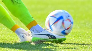 Ein Fußballspieler in grünen und gelben Stollenschuhen tritt einen Fußball mit einem bunten Design auf einem grünen Feld.