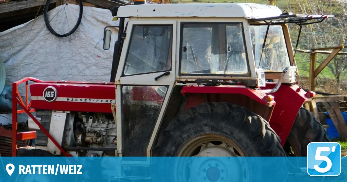 Ein roter und weißer Traktor mit der Marke Massey-Ferguson ist geparkt. Die Windschutzscheibe und die Tür sind leicht verschmutzt. Der Traktor hat einen schwarzen Reifen mit einer silbernen Felge.