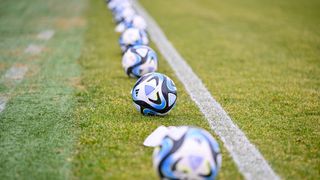 Eine Reihe von Fußballen, die auf einem Feld aufgereiht sind, mit einer weißen Linie, die sie trennt. Die Bälle haben blaue und weiße Designs.