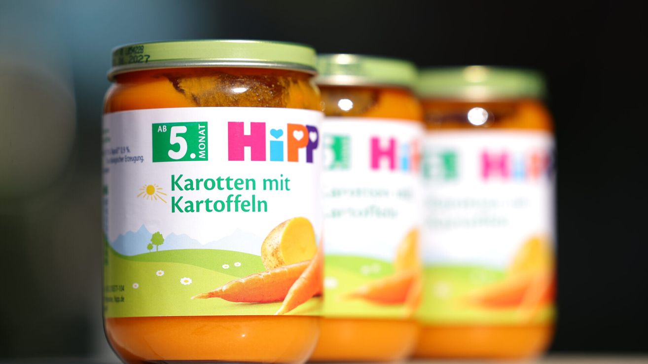 Eine Reihe von Gläsern mit Hipp-Babynahrung mit Karotten und Kartoffeln. Jedes Glas hat einen grünen Deckel und ist mit '5+ Monate' und 'Karotten mit Kartoffeln' beschriftet. Die Gläser sind mit einer pürierten orangefarbenen Mischung gefüllt.