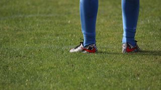 A soccer player wearing blue socks and Nike sneakers with a red and black design stands on a grassy field.