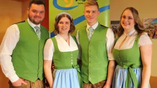Vier Personen lächeln für ein Foto in traditioneller grüner Kleidung, mit einem Schild im Hintergrund, das 'Landjugend' steht.