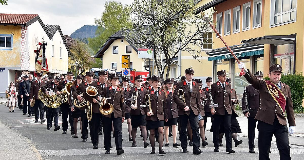 A marching band in uniforms plays brass instruments in a parade on a city street.