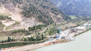 Luftaufnahme eines Berggebiets mit Fluss, Baustelle und grünem Silo.