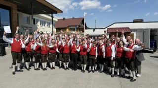 Eine Gruppe von Menschen in traditioneller Kleidung, rote Westen und schwarze Hosen tragend, posiert für ein Foto vor Gebäuden.
