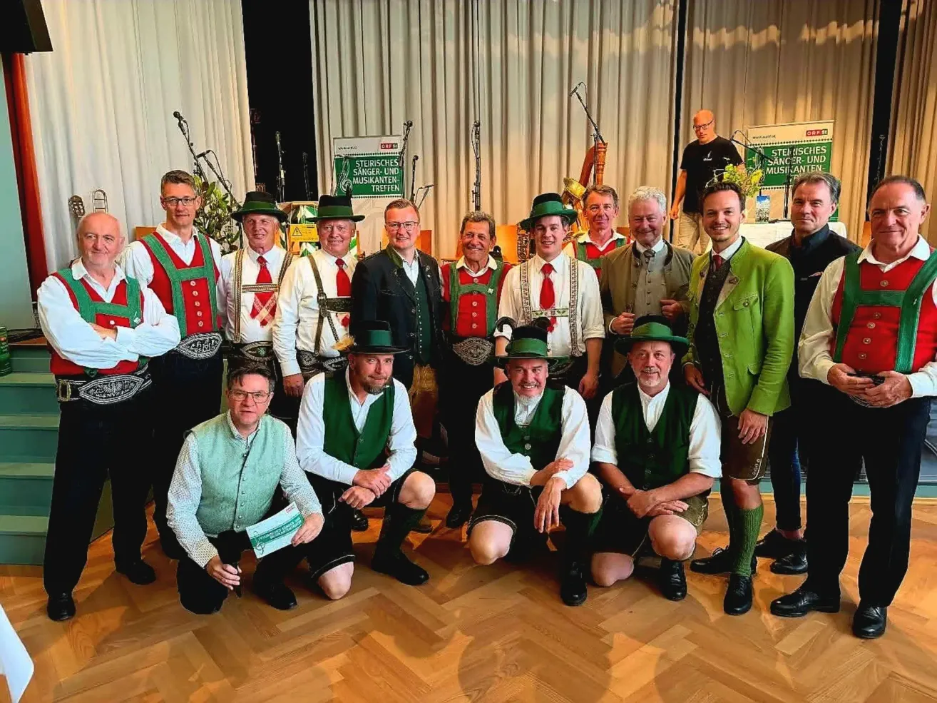 Eine Gruppe von Männern in traditioneller deutscher Kleidung posiert für ein Foto, mit einem Hintergrund, der ein Banner mit deutschem Text zeigt.