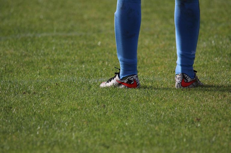 A soccer player stands on a grass field wearing blue socks and shoes with a red swoosh.
