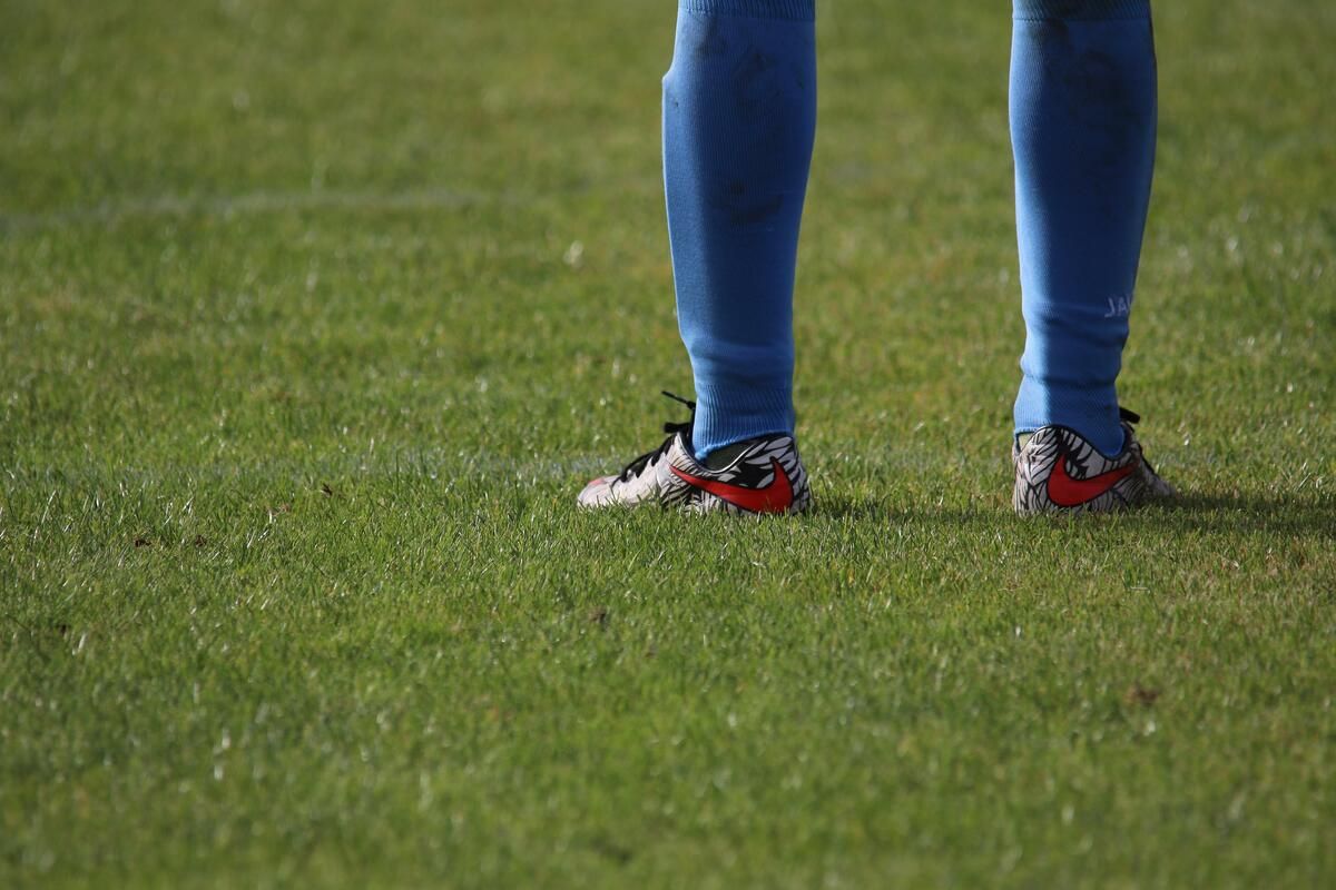 A soccer player stands on a grass field wearing blue socks and shoes with a red swoosh.