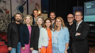 Eine Gruppe von Menschen, wahrscheinlich eine Familie, steht und lächelt und posiert wahrscheinlich für ein Foto. Sie tragen formelle Kleidung und stehen vor einer Wand mit Gemälden.