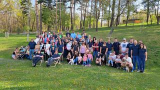 A group of people and dogs are posing for a photo in a park with trees and grass in the background.