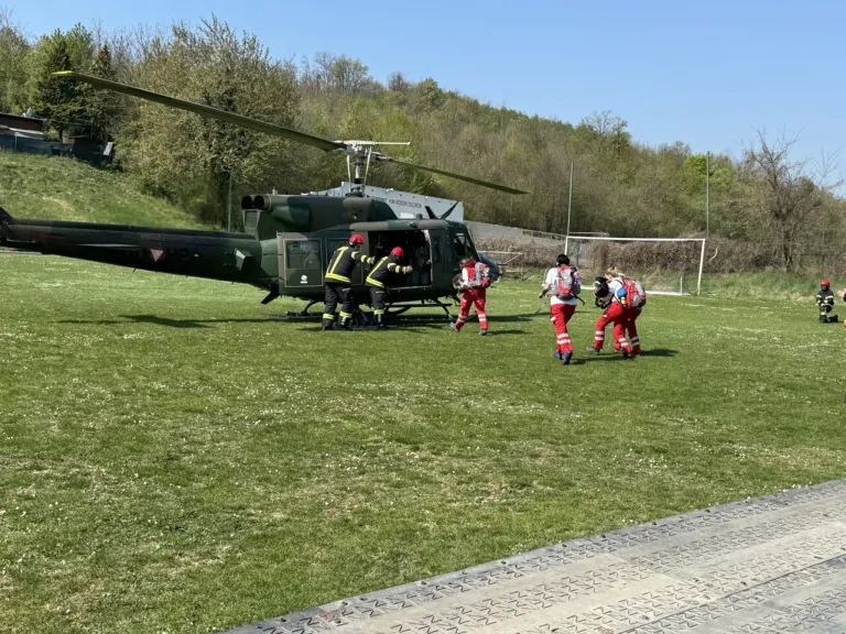 Ein Militärhubschrauber landet auf einem Feld, wobei Feuerwehrleute entladen. Einer steht in der Nähe der Tür, und mehrere andere gehen auf ein Fußballtor zu.