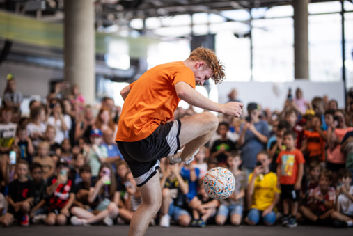 A soccer player is performing a trick with a soccer ball in front of a crowd.