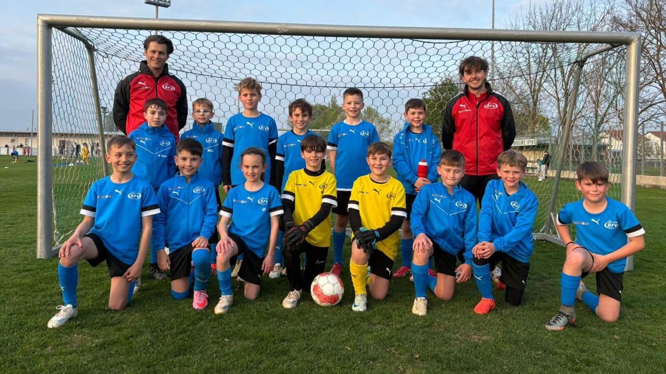Eine Jugendfußballmannschaft in blauen und gelben Trikots posiert für ein Foto vor einem Tornetz.