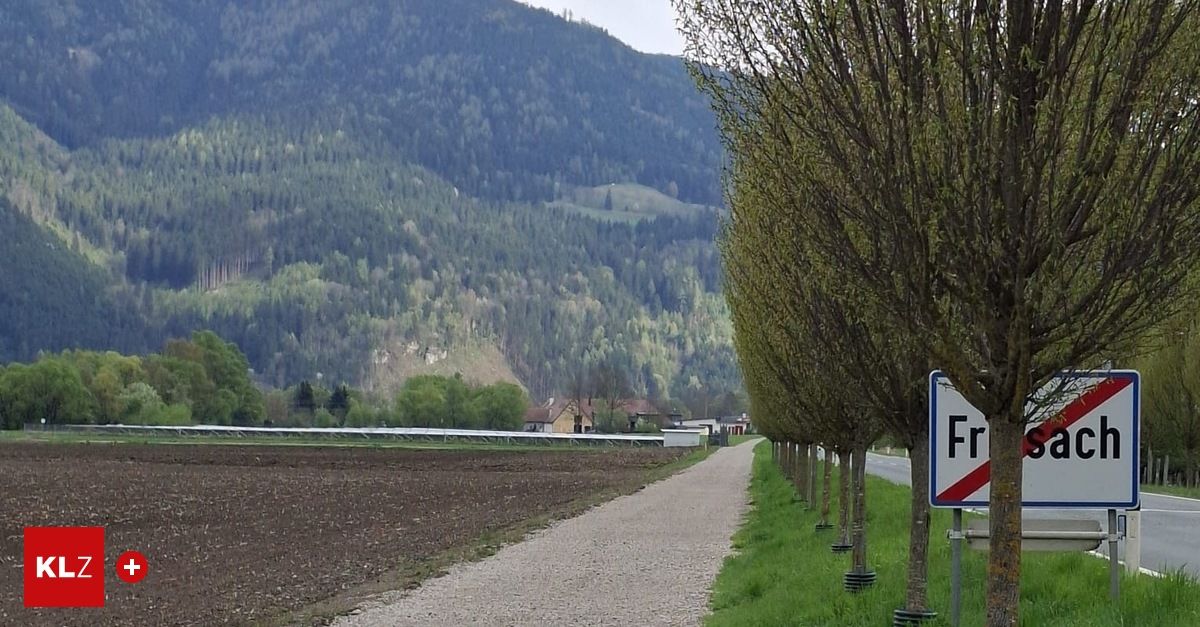 Ein Kiesweg, gesäumt von Bäumen, führt zu einem Wald. Im Hintergrund ein bewaldeter Berg. Das Schild trägt den Buchstaben 'F'.