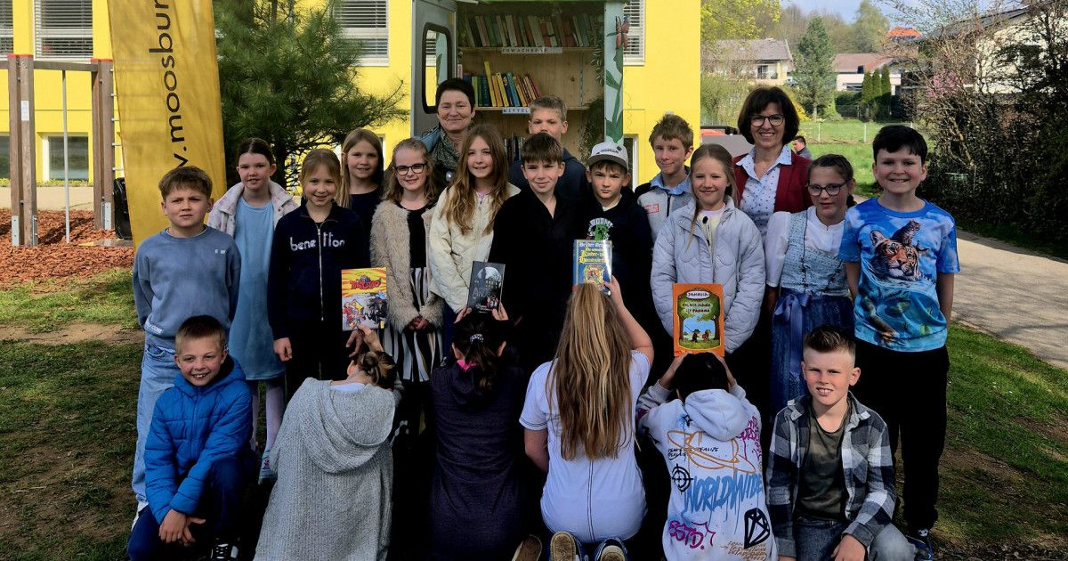 Eine Gruppe von Kindern und zwei Frauen steht vor einer mobilen Bibliothek. Die Kinder halten Bücher und schauen zur Kamera.