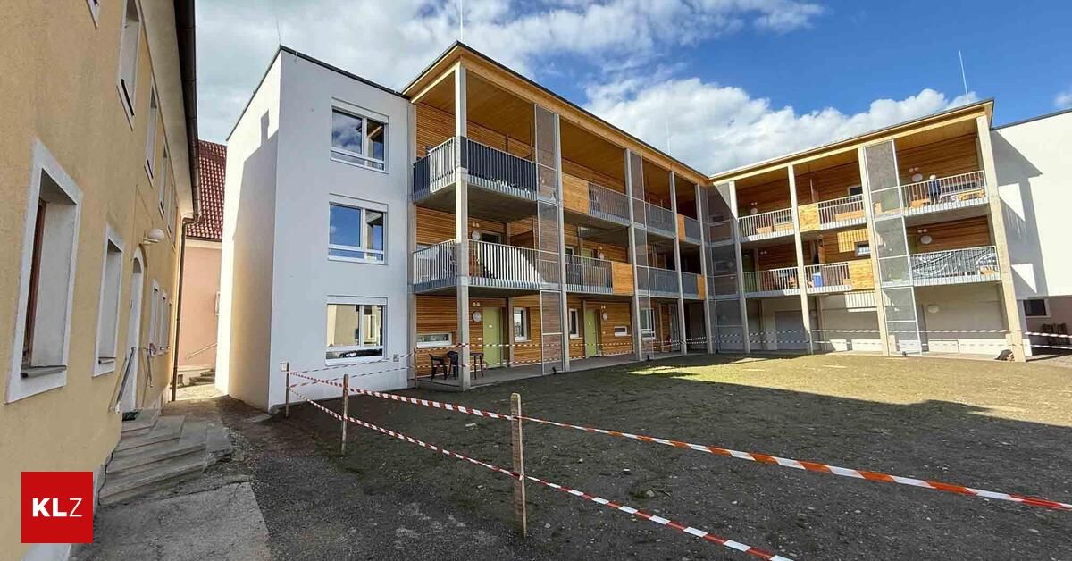 Ein modernes Apartmentgebäude mit Holzbalkonen und einem kleinen Außenbereich. Das Äußere ist weiß mit einer Mischung aus Glas- und Holzpaneelen. Es gibt Stühle und einen Tisch auf dem Balkon im Erdgeschoss.