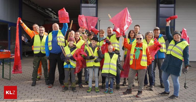 Eine Gruppe von Menschen in Warnwesten hält Stöcke und Flaggen und steht vor einem Gebäude.