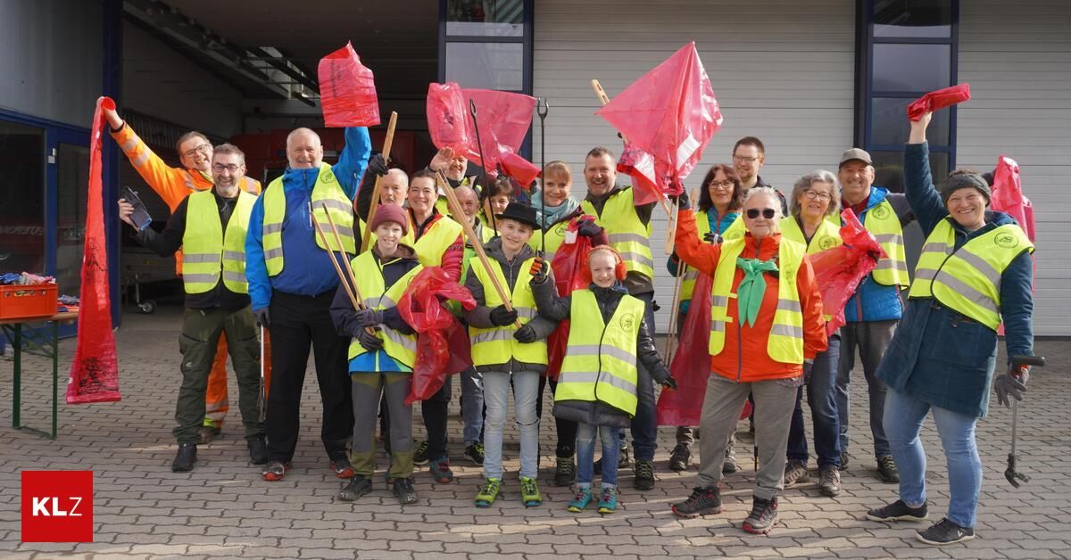 Eine Gruppe von Menschen in Warnwesten hält Stöcke und Flaggen und steht vor einem Gebäude.