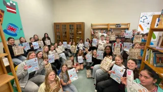 Eine Gruppe von Schülern versammelt sich in einem Klassenzimmer, hält Urkunden und lächelt, während einige Bücher mit dem Titel 'Roll' halten.