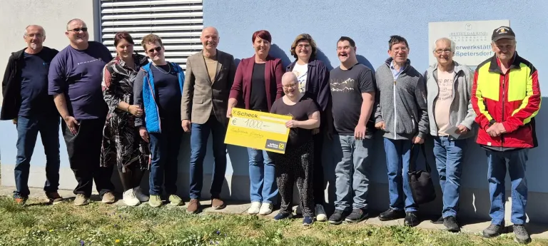 Eine Gruppe von Menschen steht zusammen und hält einen großen gelben Scheck. Die Frau in der Mitte hält einen Scheck über 1000 Euro. Sie alle sehen glücklich und lächelnd aus.