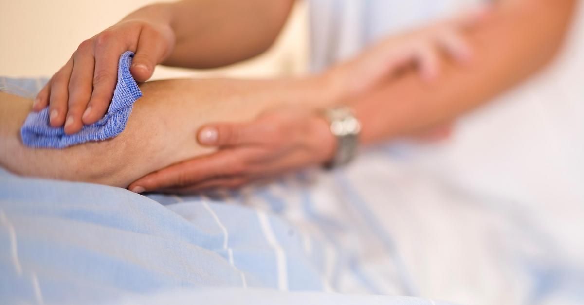 A person lying down with a blue cloth on their leg, another person holding their leg with a watch on their wrist.