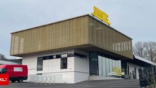 Außenansicht eines modernen Gebäudes mit einem gelben Schild, das oben und am Eingang 'OAMTC' steht, mit einem roten Lastwagen, der davor geparkt ist.