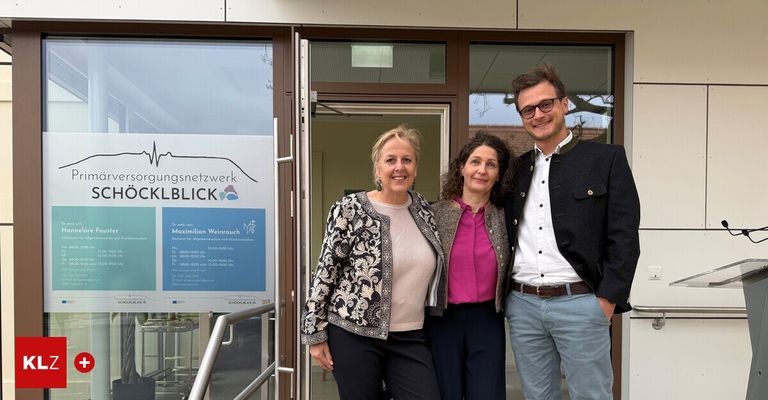 Three people stand outside a building entrance, smiling for a photo. The woman on the left wears a patterned jacket, the middle woman a pink shirt, and the man on the right glasses and a black coat. A sign reads 'Maximilian Weinrauch' and 'CKLBLICK' above the entrance.