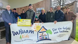 Eine Gruppe von Menschen posiert hinter einem Banner für DaHuan 4 Kids und hält ein Schild mit einem Spendenbetrag von 1.000 €.